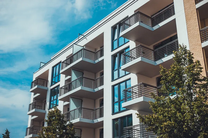 Moderne leilighetsbygg med hvit fasade, glassvinduer og balkonger mot blå himmel